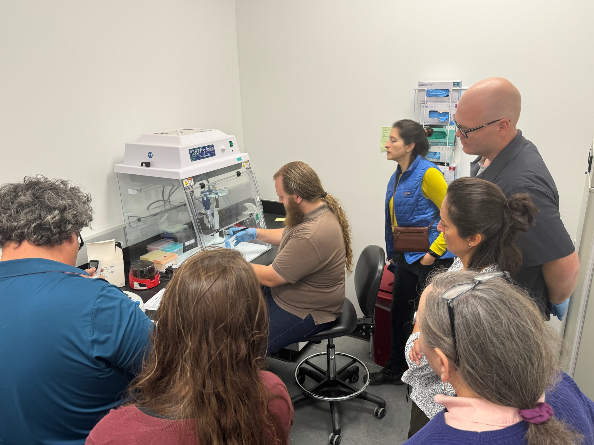 A man demostrating a lab technique under a sterile field to others.